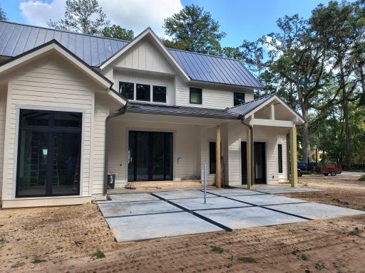 Modern two-story house with a porch and unfinished concrete patio, surrounded by trees.