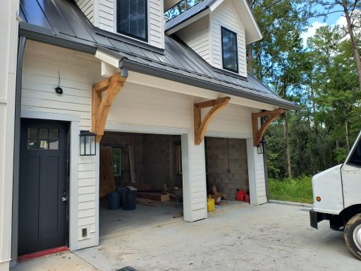 Modern house exterior with two garage doors and wooden supports, surrounded by greenery.